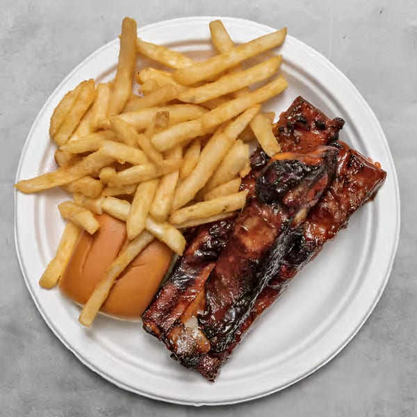 A white plate holds a serving of BBQ ribs, golden fries, and a soft bun.