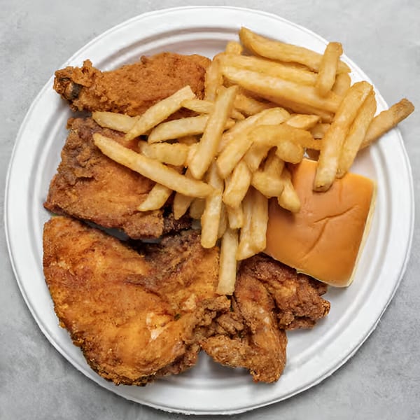 A white plate holds golden-brown fried chicken pieces, a pile of french fries, and a dinner roll.